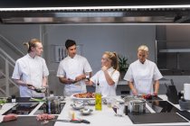 Um grupo de chefs brancos cozinhando, conversando e olhando uns para os outros. Aula de culinária em uma cozinha de restaurante. — Fotografia de Stock
