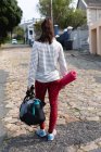 Rückansicht einer fitten Kaukasierin auf dem Weg zum Fitnesstraining an einem bewölkten Tag mit Sporttasche und Yogamatte — Stockfoto