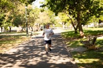 Vista frontal de un atlético hombre mayor caucásico haciendo ejercicio en un parque en un día soleado, corriendo en una pista - foto de stock