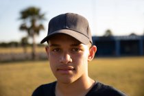Porträt eines Baseballspielers gemischter Rasse, der eine Mannschaftsuniform und eine Mütze trägt, auf einem Baseballfeld steht und in eine Kamera blickt — Stockfoto