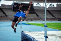 Vista laterale di un atleta maschio di razza mista che pratica in uno stadio sportivo, facendo un salto in alto. Allenamento di atletica leggera nello stadio. — Foto stock