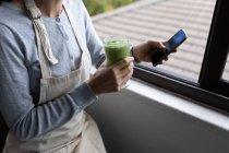 Mid section of woman spending time at home, drinking smoothie, using her smartphone. Lifestyle at home isolating, social distancing in quarantine lockdown during coronavirus covid 19 pande — Stock Photo