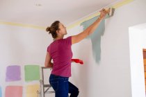 Caucasian woman spending time at home self isolating and social distancing in quarantine lockdown during coronavirus covid 19 epidemic, painting the walls of her home. — Stock Photo