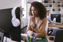 Eine Geschäftsfrau mit gemischter Rasse, die in einem modernen Büro arbeitet, am Schreibtisch sitzt und einen Computer benutzt, während ihre Geschäftskollegen im Hintergrund arbeiten. — Stockfoto