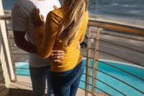 Vista de mitad de la sección de la pareja de pie en un balcón, abrazando. Distanciamiento social y autoaislamiento en cuarentena. - foto de stock