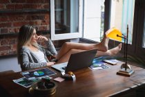 Auto-isolement en quarantaine. vue latérale d'une jeune femme caucasienne, assise dans son bureau à la maison, utilisant un ordinateur portable tout en travaillant. — Photo de stock