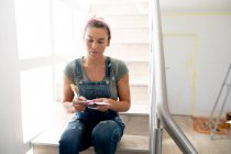 Caucasian woman spending time at home self isolating and social distancing in quarantine lockdown during coronavirus covid 19 epidemic, sitting on stairs, preparing for paint the walls of her house. — Stock Photo