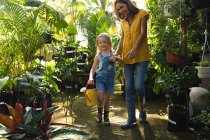 Una donna caucasica e sua figlia godono del tempo insieme in un giardino soleggiato, guardando le piante, la figlia che tiene un annaffiatoio — Foto stock