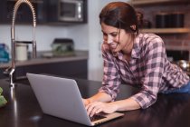 Mixed race woman spending time at home self isolating and social distancing in quarantine lockdown during coronavirus covid 19 epidemic, using laptop in kitchen. — Stock Photo