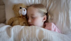 High angle front view close up of a Caucasian girl enjoying free time at home, sleeping in her bed, next to her teddy bear — Stock Photo