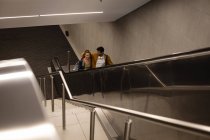 Front high angle view of a Caucasian couple out and about in the city, going up in underground station with an escalator, smiling and embracing. — Stock Photo