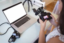 Femme vlogger caucasienne à la maison, dans son salon en utilisant une caméra et un ordinateur portable pour préparer son blog en ligne. Distance sociale et isolement personnel en quarantaine. — Photo de stock