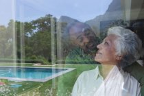 Felice anziano pensionato coppia afroamericana a casa, guardarsi e sorridere, riflesso in una finestra con vista sul loro giardino con piscina, coppia a casa isolandosi durante il coronavirus covid19 pandemia — Foto stock