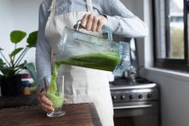 Mid section of woman spending time at home, pouring smoothie. Lifestyle at home isolating, social distancing in quarantine lockdown during coronavirus covid 19 pandemic. — Stock Photo