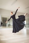 Кавказская привлекательная балетная танцовщица с рыжими волосами танцует балет, одета в черное, длинное платье, готовится к балетному классу в яркой студии, концентрируется на своих упражнениях. — стоковое фото