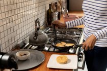 Mitte einer Frau zu Hause in der Küche, die am Herd steht und Pfannkuchen in einer Pfanne kocht — Stockfoto