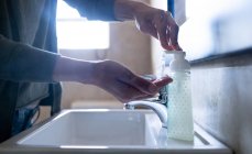 Закрытие рук женщины дома в ванной в дневное время моет руки в раковине с помощью жидкого мыла, защиты от коронавируса Covid-19 инфекции и пандемии. Социальное дистанцирование и самоизоляция в карантинной изоляции — стоковое фото