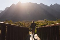 Rückansicht einer kaukasischen Frau, die bei einem Ausflug in die Berge Spaß hat, auf einer Brücke steht und an einem sonnigen Tag die Aussicht genießt — Stockfoto