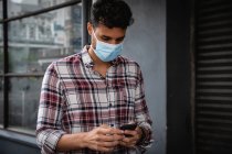 Nahaufnahme eines kaukasischen Mannes mit kariertem Hemd und Gesichtsmaske gegen Luftverschmutzung und Covid19 Coronavirus, der mit seinem Smartphone durch die Straßen der Stadt läuft. — Stockfoto