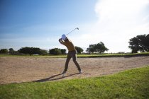Попереду Кавказький чоловік на полі для гольфу в сонячний день з блакитним небом, готуючись до удару м'ячем. — стокове фото