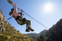 Visão traseira de baixo ângulo da mulher caucasiana desfrutando do tempo na natureza, tirolesa em um dia ensolarado nas montanhas. Diversão aventura férias fim de semana. — Fotografia de Stock