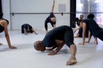 Seitenansicht einer multiethnischen Gruppe fitter männlicher und weiblicher moderner Tänzer in schwarzen Outfits, die während eines Tanzkurses in einem hellen Studio eine Tanzroutine praktizieren, einen Kreis bilden und sich strecken. — Stockfoto