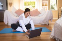 Кавказька жінка-блогер вдома у вітальні, практикує йогу і за допомогою ноутбука. Соціальна дистанція і самоізоляція в карантинному блокуванні.. — стокове фото