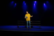 Frontansicht eines kaukasischen Teenagers, der während der Proben für eine Aufführung in einem leeren Schultheater auf der Bühne steht und ein Drehbuch hält — Stockfoto