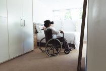 Femme de race mixte âgée profitant de son temps à la maison, de la distance sociale et de l'isolement personnel en quarantaine, assise sur un fauteuil roulant, portant des lunettes vr — Photo de stock