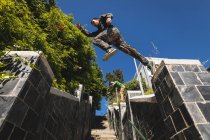 Side low angle view of a Caucasian man practicing parkour by the building in a city on a sunny day, jumping on stairs handrail. — Stock Photo