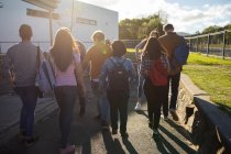 Вид ззаду на багатоетнічну групу студентів-чоловіків і жінок-підлітків, які розмовляють під час прогулянки по шкільних місцях — стокове фото