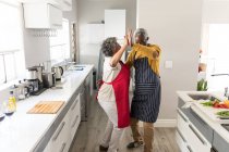 Старшая афроамериканская пара проводит время дома вместе, социальное дистанцирование и самоизоляция в карантинной изоляции во время эпидемии коронавируса 19, танцует на кухне — стоковое фото