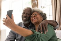 Un couple afro-américain âgé passe du temps à la maison ensemble, la distance sociale et l'isolement personnel en quarantaine pendant l'épidémie de coronavirus covid 19, la femme tenant un smartphone et prenant un selfie — Photo de stock