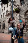 Передній вид на кавказьку та змішану расу дівчат, які проводять час разом у сонячний день, дівчина стоїть на тротуарі і відбирає собі та її друга, що чіпляється за вуличну лампу.. — стокове фото
