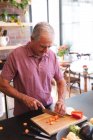 Happy retired senior Caucasian man at home in the kitchen on a sunny day, standing at the worktop chopping vegetables on a chopping board and smiling, self isolating during coronavirus covid19 pandemic — Stock Photo