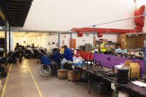 Gruppe behinderter afroamerikanischer männlicher Arbeiter in einer Werkstatt einer Fabrik, die Rollstühle herstellt, an einer Werkbank sitzend, Teile eines Produkts montierend, zwei im Rollstuhl sitzend, einer mit Krücken — Stockfoto