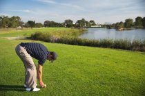 Side view of a Caucasian man at a golf course on a sunny day with blue sky, placing a golf ball on the grass — Stock Photo