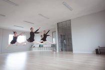 A group of Caucasian female attractive ballet dancers in black outfits practicing during a ballet class in a bright studio, dancing and jumping in the air in unison. — Stock Photo