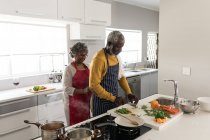 Un couple afro-américain âgé passe du temps à la maison ensemble, la distance sociale et l'isolement personnel en quarantaine pendant l'épidémie de coronavirus covid 19, debout dans la cuisine pour préparer la nourriture — Photo de stock
