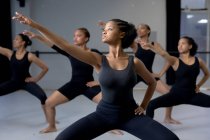 Вид спереди на многонациональную группу современных женщин-танцовщиц в черных нарядах, практикующих танцевальную программу во время урока танцев в яркой студии, расправляющих руки. — стоковое фото