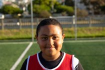 Portrait close up of a confident mixed race boy soccer player wearing a team strip, standing on a playing field in the sun, looking to camera and smiling — Stock Photo