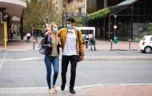 Vorderansicht eines kaukasischen Paares, das tagsüber in den Straßen der Stadt unterwegs ist und Gesichtsmasken gegen Luftverschmutzung und Covid19 Coronavirus trägt.. — Stockfoto