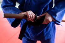 Vue de face de la section médiane du judoka portant du judogi bleu, tenant du judo jo stick en bois, debout dans la salle de gym pendant un entraînement de judo. — Photo de stock