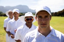 Vista frontal close-up de uma equipe de críquete masculino multi-étnico adolescente vestindo brancos, de pé em campo juntos em uma fileira olhando direto para a câmera — Fotografia de Stock