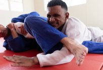 Vue de face rapprochée d'un entraîneur de judo masculin métis et d'un judoka masculin métis adolescents portant du judoka bleu et blanc, pratiquant le judo lors d'un entraînement dans une salle de gym. — Photo de stock