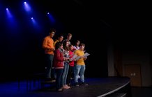 Vista laterale di un gruppo multietnico di coristi adolescenti maschili e femminili che tengono spartiti e cantano in piedi sul palco di un teatro scolastico durante le prove di uno spettacolo — Foto stock