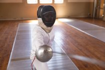 Caucasian sportswoman wearing protective fencing outfit during a fencing training session, preparing for a duel, holding an epee and aiming. Fencers training at a gym. — Stock Photo