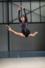 Передній вигляд підліткової змішаної раси гімнастка, яка виступає в спортзалі, стрибає і робить розкол, одягнена в чорно-фіолетовий леопард — стокове фото