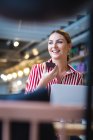 Una donna d'affari caucasica con i capelli corti, seduta a un tavolo all'interno di un caffè, che parla sul suo smartphone e sorride, indossa vestiti alla moda — Foto stock