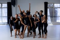 Вид спереду на багатоетнічну групу сучасних танцюристів, які носять чорні вбрання, які практикують танцювальну рутину під час танцювального заняття в яскравій студії, стоять разом, посміхаючись і дивлячись прямо в камеру . — стокове фото